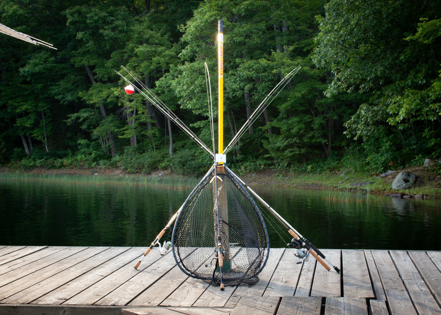 Home Fishing rods and a net rest against a pole on a wooden dock.